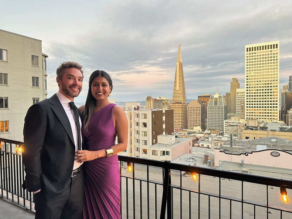 Dressed up on a rooftop at a friend’s wedding, the San Francisco skyline behind them